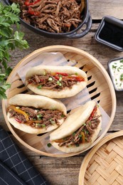 Delicious gua bao in bamboo steamer on wooden table, flat lay