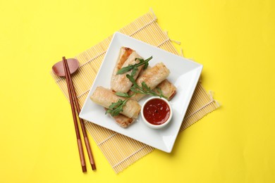 Photo of Fried spring rolls, arugula and sauce served on yellow table, top view