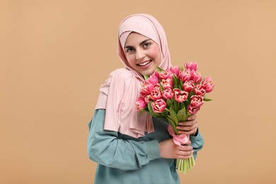 Photo of Happy woman in hijab with beautiful bouquet on beige background