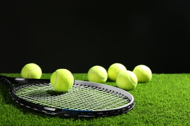 Photo of Tennis racket and balls on green grass against dark background. Space for text