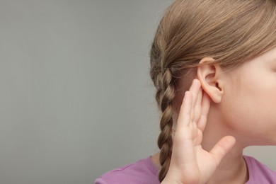 Photo of Little girl with hearing problem on grey background, closeup. Space for text