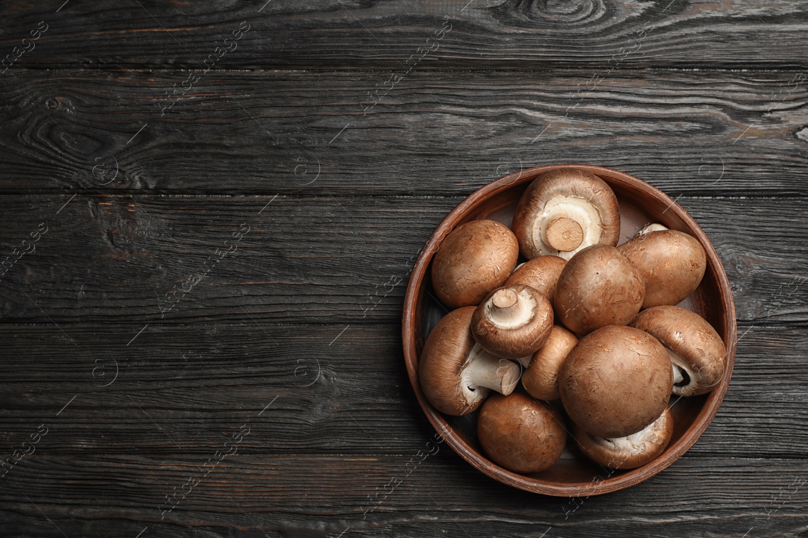 Photo of Bowl with fresh champignon mushrooms on wooden table, top view. Space for text