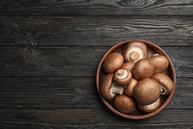 Bowl with fresh champignon mushrooms on wooden table, top view. Space for text