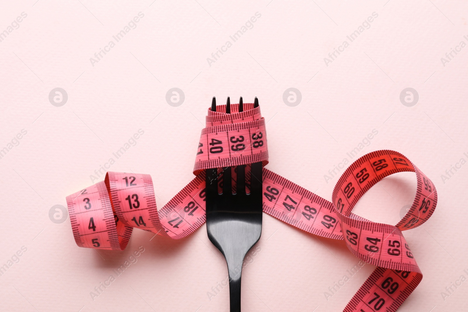 Photo of Fork with measuring tape on pale pink background, top view. Diet concept