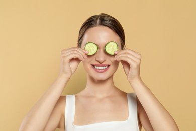 Photo of Young woman with cucumber slices on beige background. Eye skin care