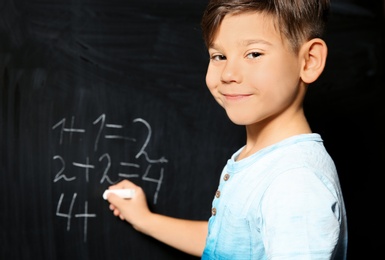 Little child with chalk doing math at blackboard