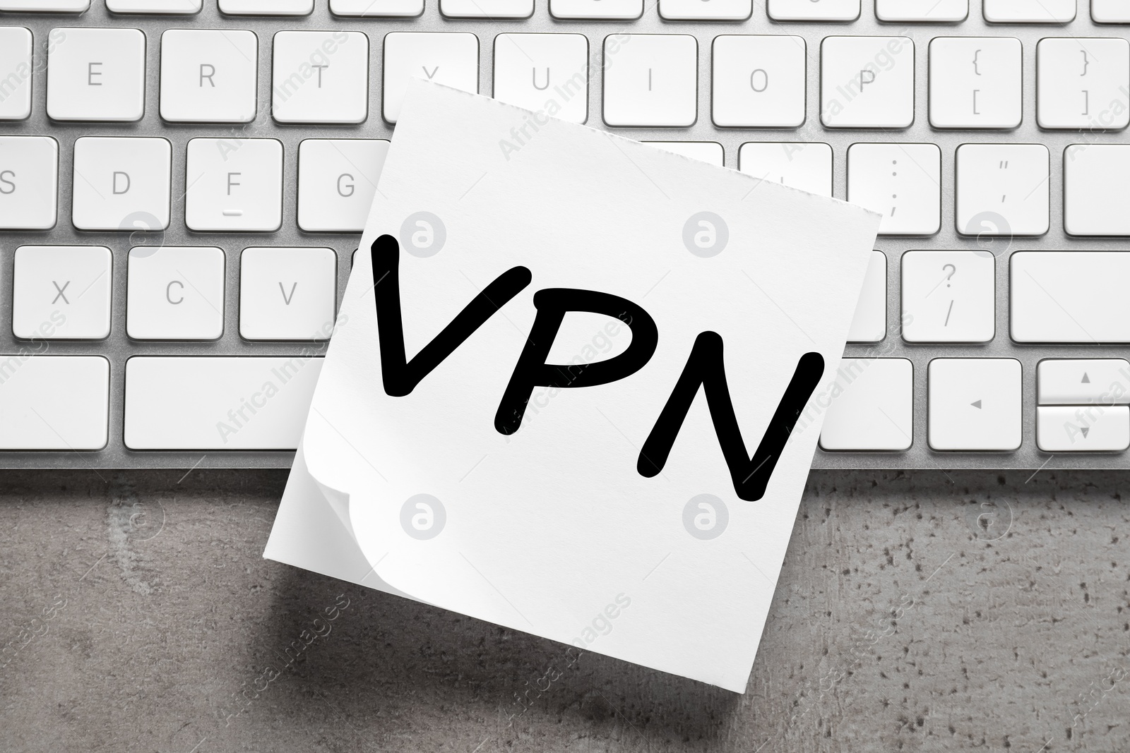 Photo of Paper sheet with acronym VPN (Virtual Private Network) and keyboard on grey table, top view