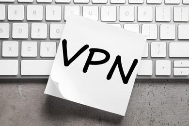 Photo of Paper sheet with acronym VPN (Virtual Private Network) and keyboard on grey table, top view