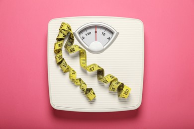 Weigh scales and measuring tape on pink background, top view. Overweight concept