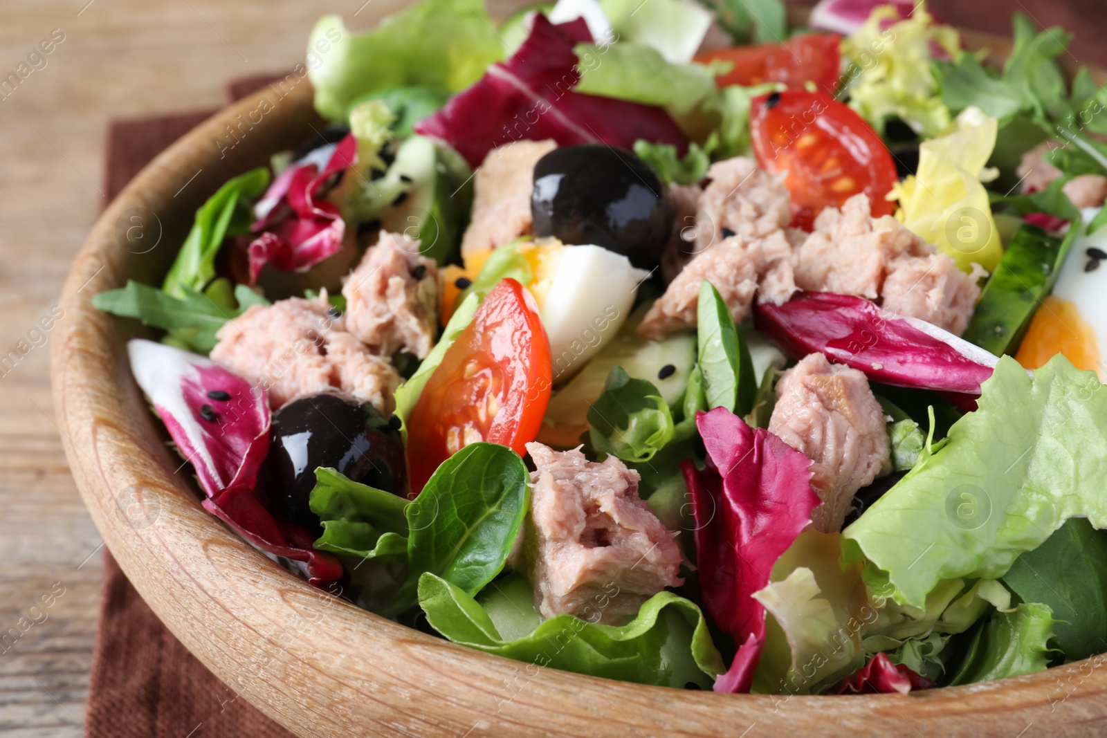 Photo of Bowl of delicious salad with canned tuna and vegetables on wooden table, closeup