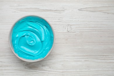Photo of Bowl of cream with light blue food coloring on white wooden table, top view. Space for text