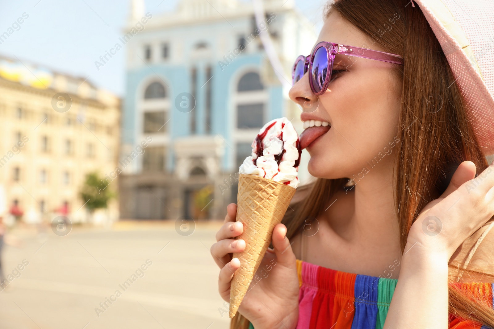 Photo of Young happy woman eating ice cream on city street. Space for text