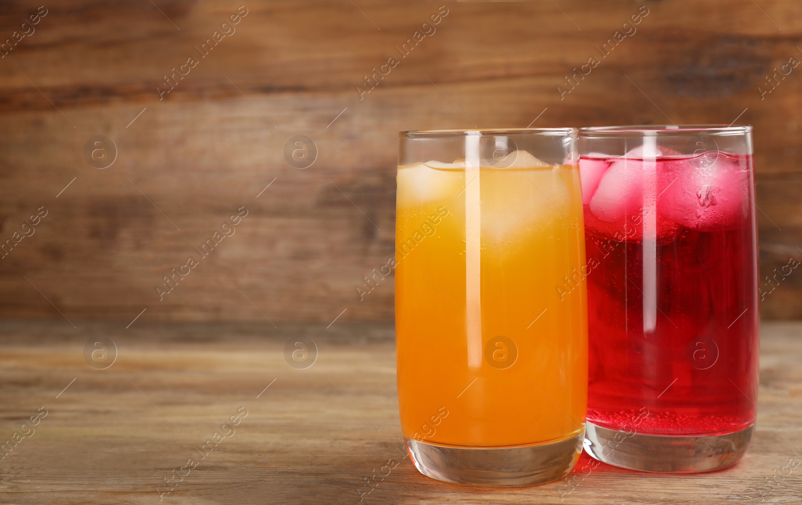 Photo of Glasses of different refreshing soda water with ice cubes on wooden table. Space for text