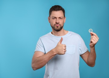 Photo of Handsome man with condom showing thumb up on light blue background. Space for text