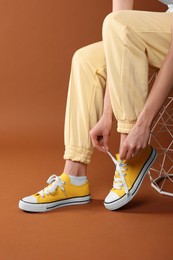 Woman tying shoelace of classic old school sneaker on brown background, closeup