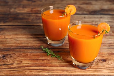 Photo of Glasses of tasty carrot juice on wooden table, closeup. Space for text