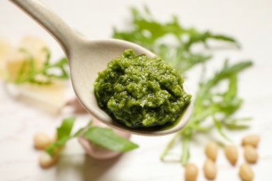 Photo of Spoon of tasty arugula pesto on blurred background, closeup