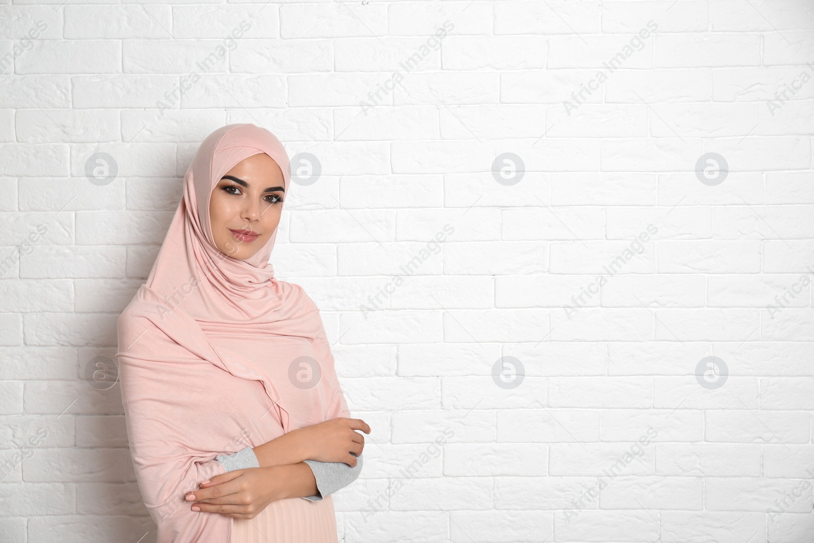 Photo of Portrait of young Muslim woman in hijab against brick wall. Space for text