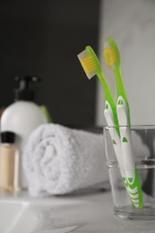 Photo of Light green toothbrushes in glass holder on washbasin indoors
