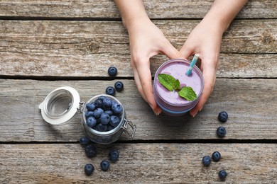 Woman with tasty blueberry smoothie at wooden table, top view