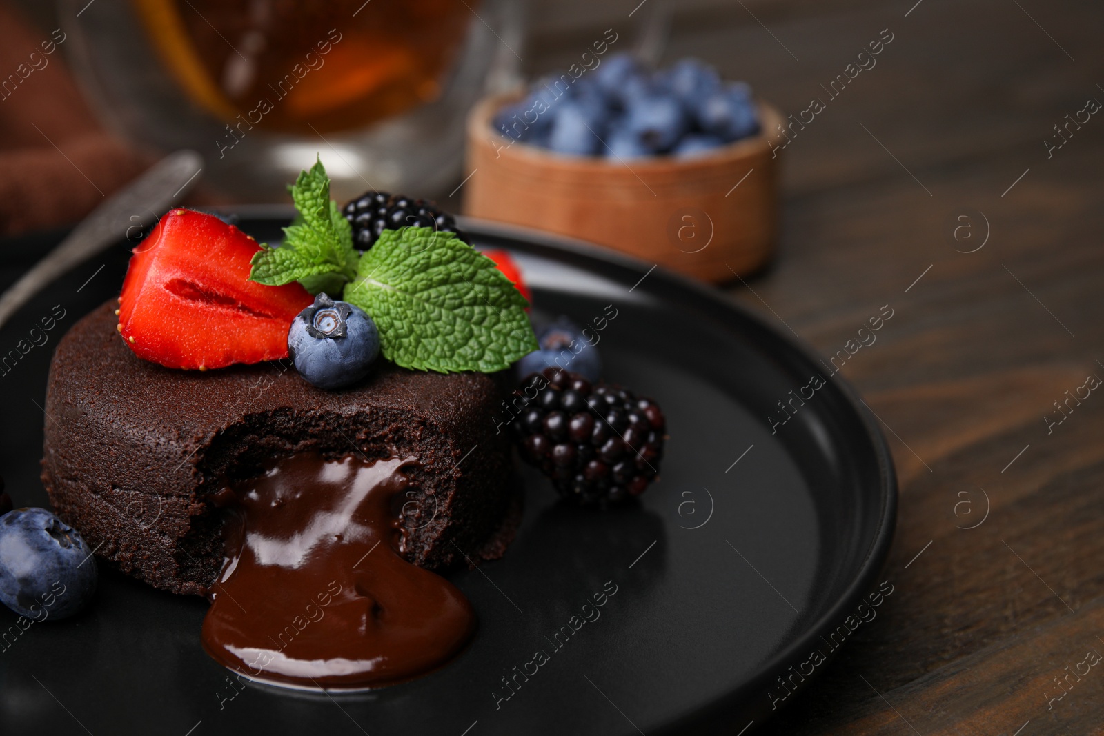 Photo of Plate with delicious chocolate fondant, berries and mint on wooden table, closeup