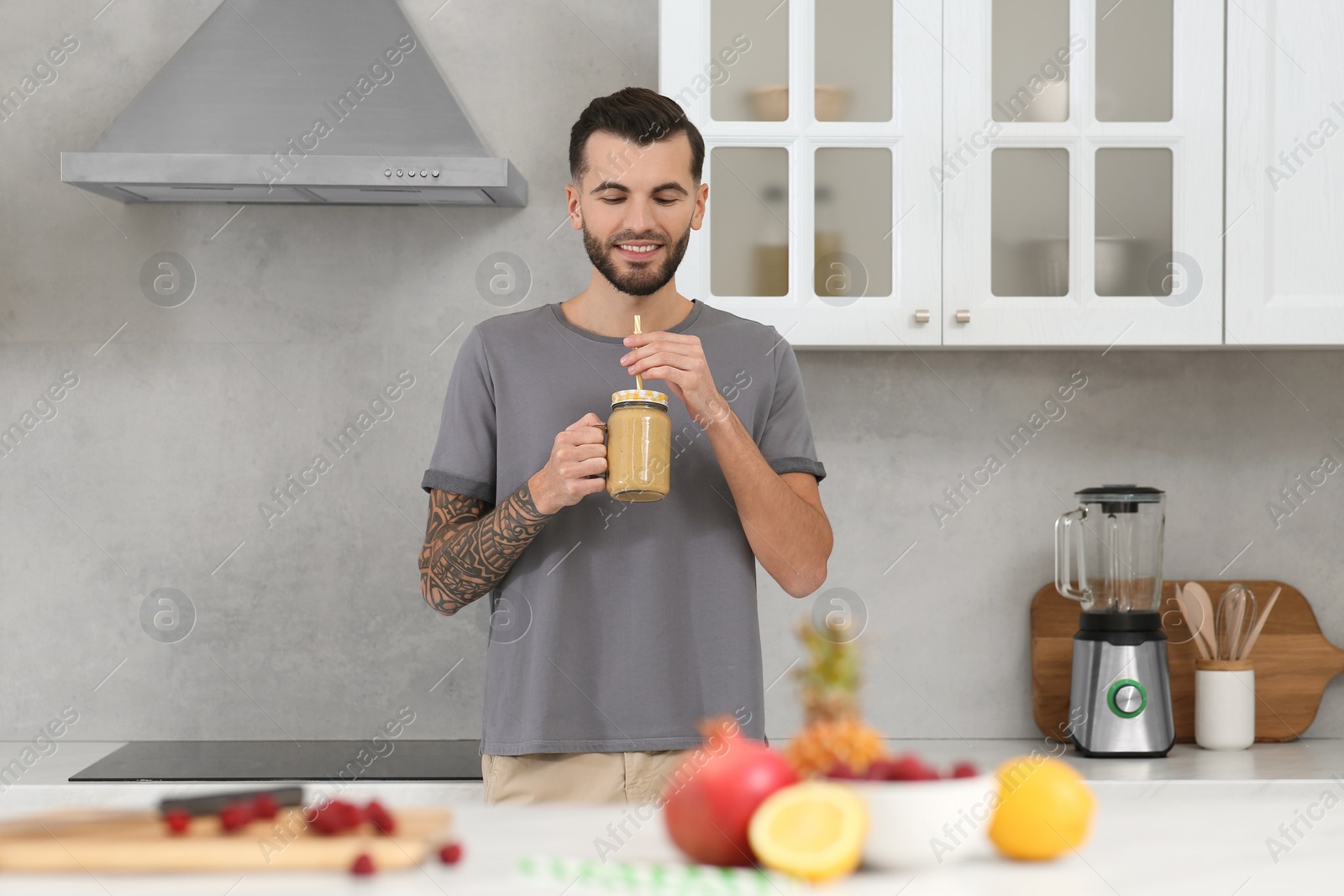 Photo of Handsome man with delicious smoothie in kitchen