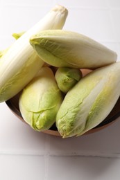 Photo of Fresh raw Belgian endives (chicory) in bowl on white tiled table, closeup