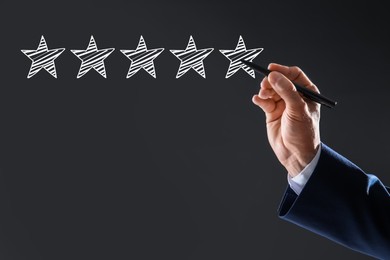 Image of Man pointing at icons of five stars on dark grey background, closeup. Quality rating