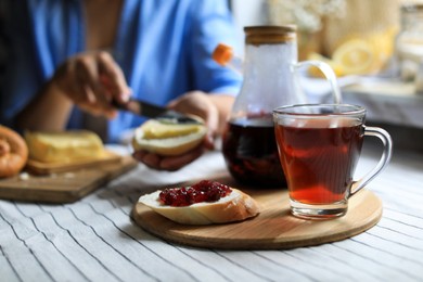 Photo of Woman spreading butter onto bread at table indoors, focus on aromatic tea