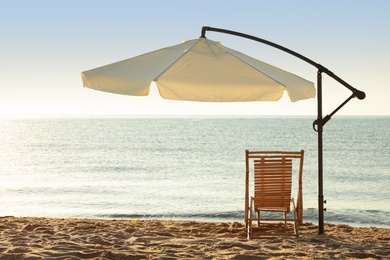 Photo of Wooden deck chair and outdoor umbrella on sandy beach. Summer vacation