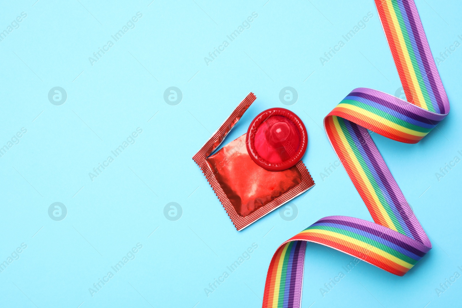 Photo of Red condom and rainbow ribbon on light blue background, flat lay. LGBT concept