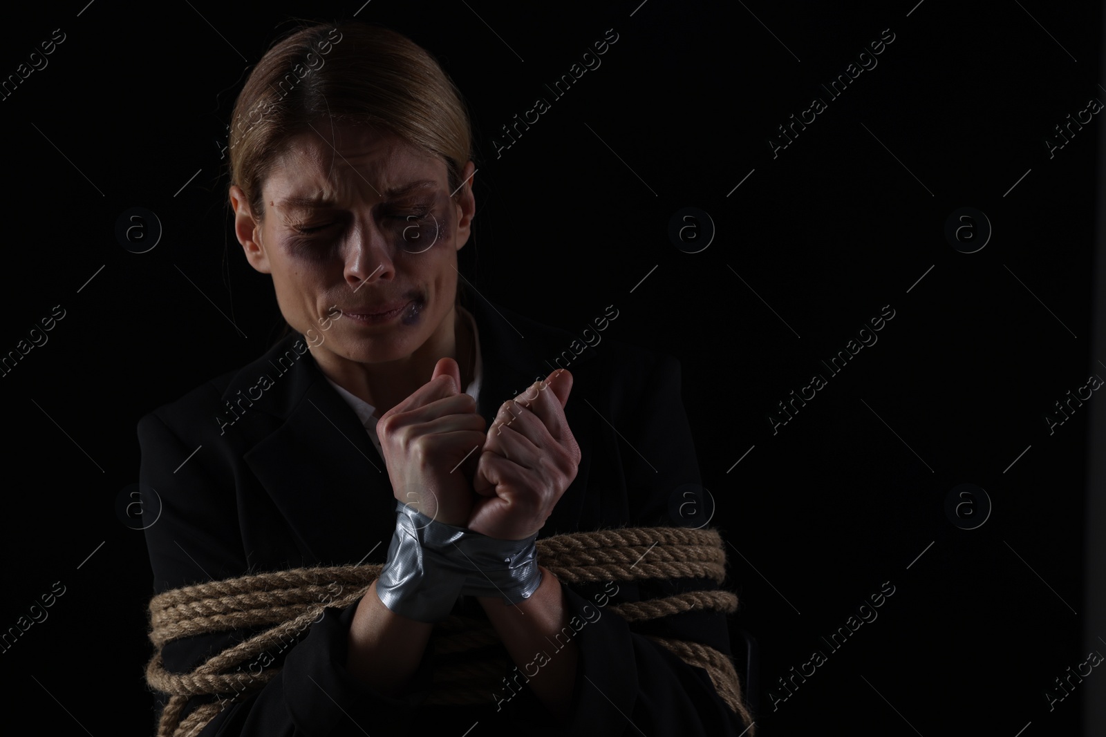 Photo of Scared woman tied up and taken hostage on dark background. Space for text