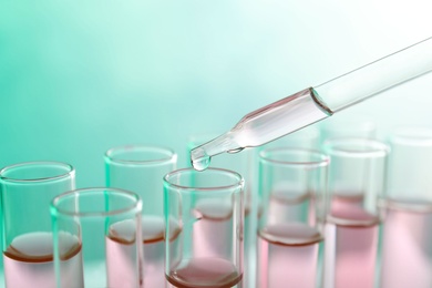 Photo of Dropping sample into test tube with liquid on color background, closeup