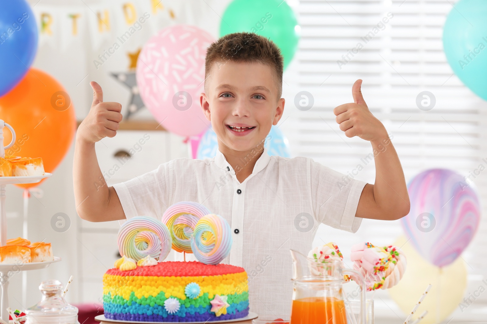 Photo of Happy boy at table with treats in room decorated for birthday party