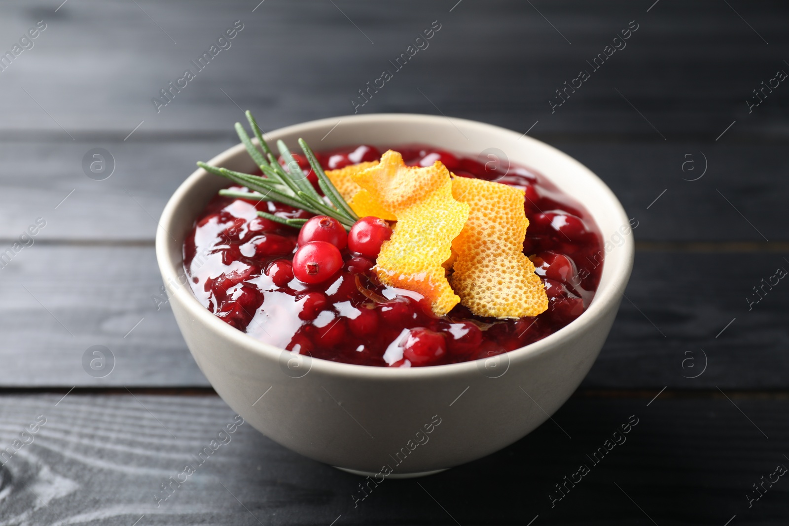 Photo of Fresh cranberry sauce, rosemary and orange peel in bowl on black wooden table, closeup