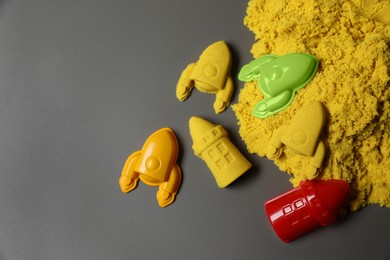 Different figures made of yellow kinetic sand and plastic toys on grey background, flat lay. Space for text