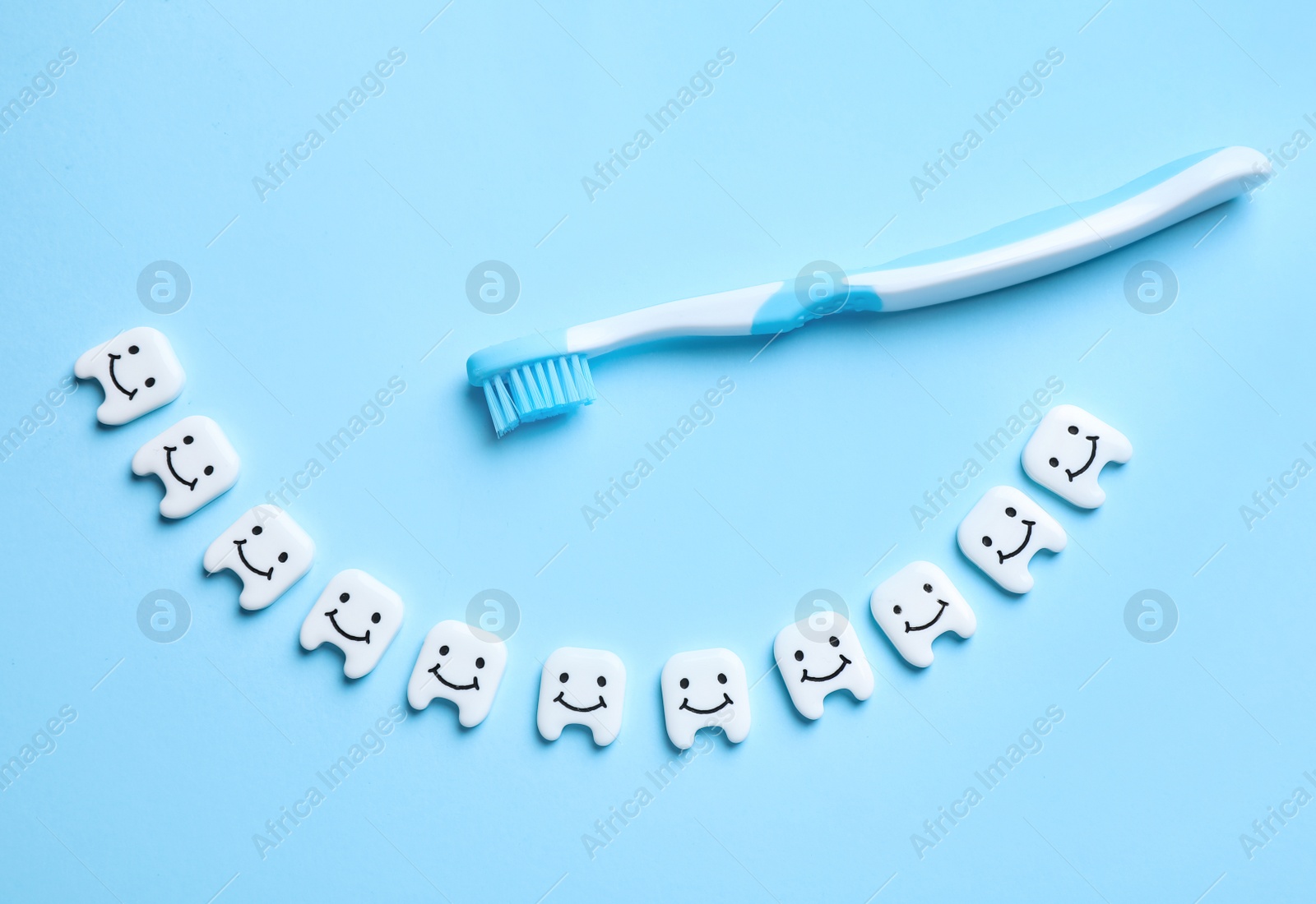 Photo of Small plastic teeth with happy faces and toothbrush on light blue background, flat lay