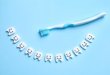 Photo of Small plastic teeth with happy faces and toothbrush on light blue background, flat lay