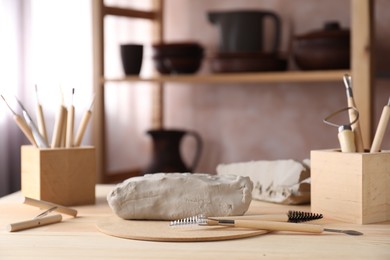 Photo of Clay and set of modeling tools on wooden table in workshop