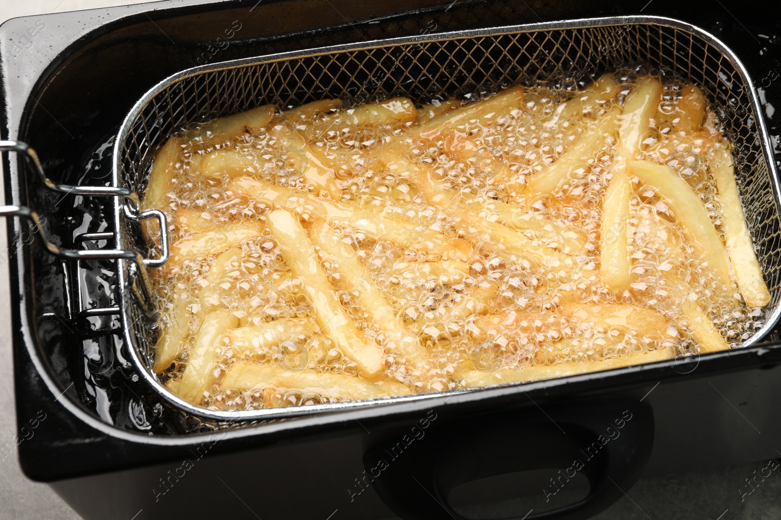 Photo of Cooking delicious french fries in hot oil, closeup