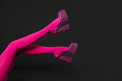Woman wearing pink tights and high heeled shoes with platform and square toes on black background, closeup. Space for text