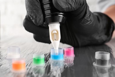 Photo of Tattoo artist with professional machine and colorful inks at table, closeup