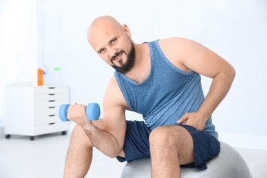 Overweight man doing exercise with dumbbell in gym