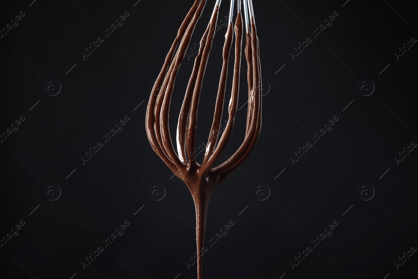 Photo of Chocolate cream flowing from whisk on black background, closeup