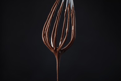 Photo of Chocolate cream flowing from whisk on black background, closeup