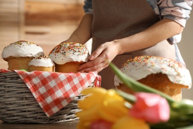 Photo of Woman putting traditional Easter cakes in basket indoors, closeup