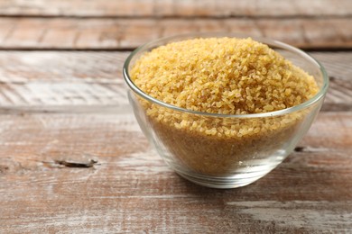 Raw bulgur in bowl on wooden table, closeup. Space for text