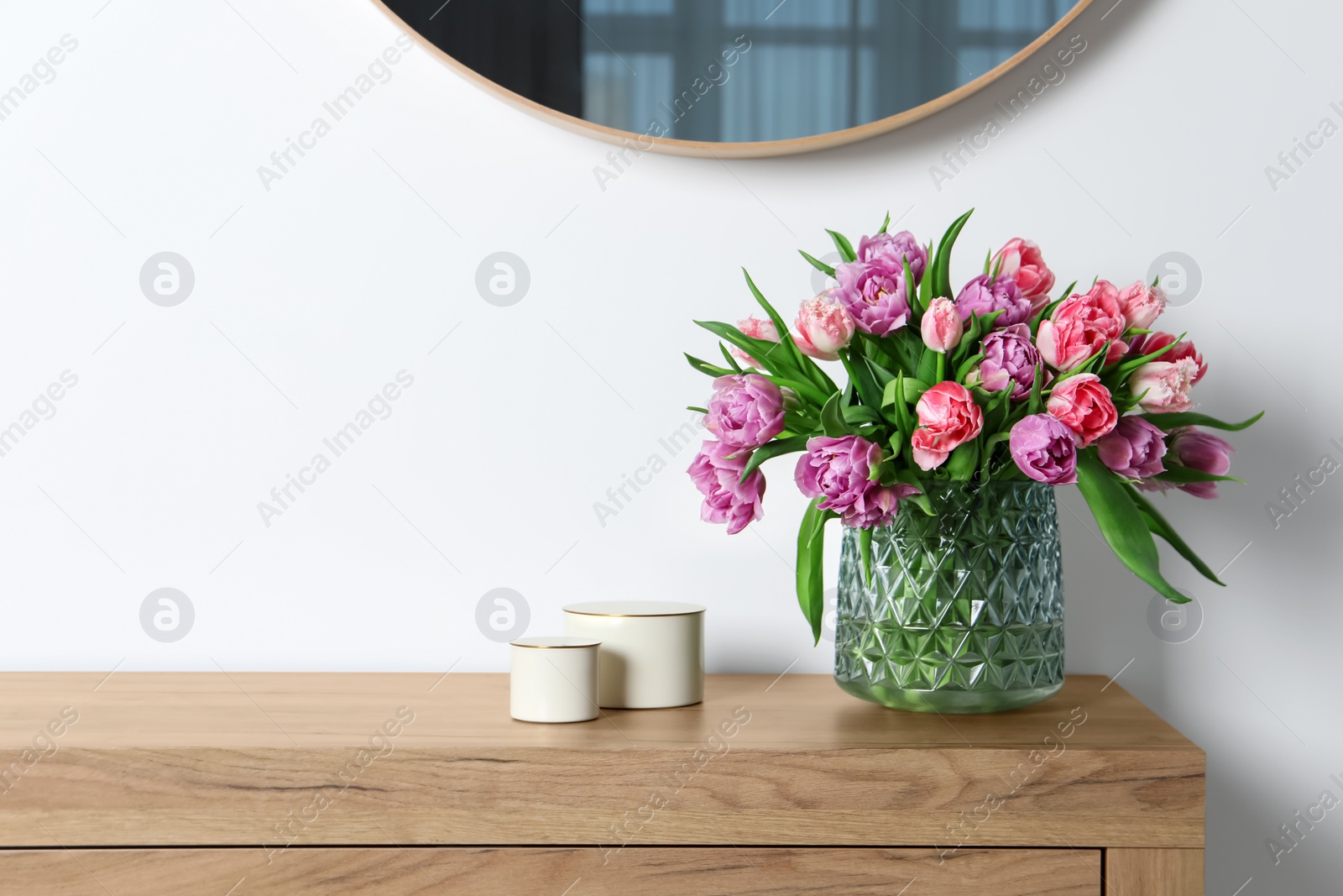 Photo of Beautiful bouquet of colorful tulip flowers on wooden chest of drawers near white wall. Space for text