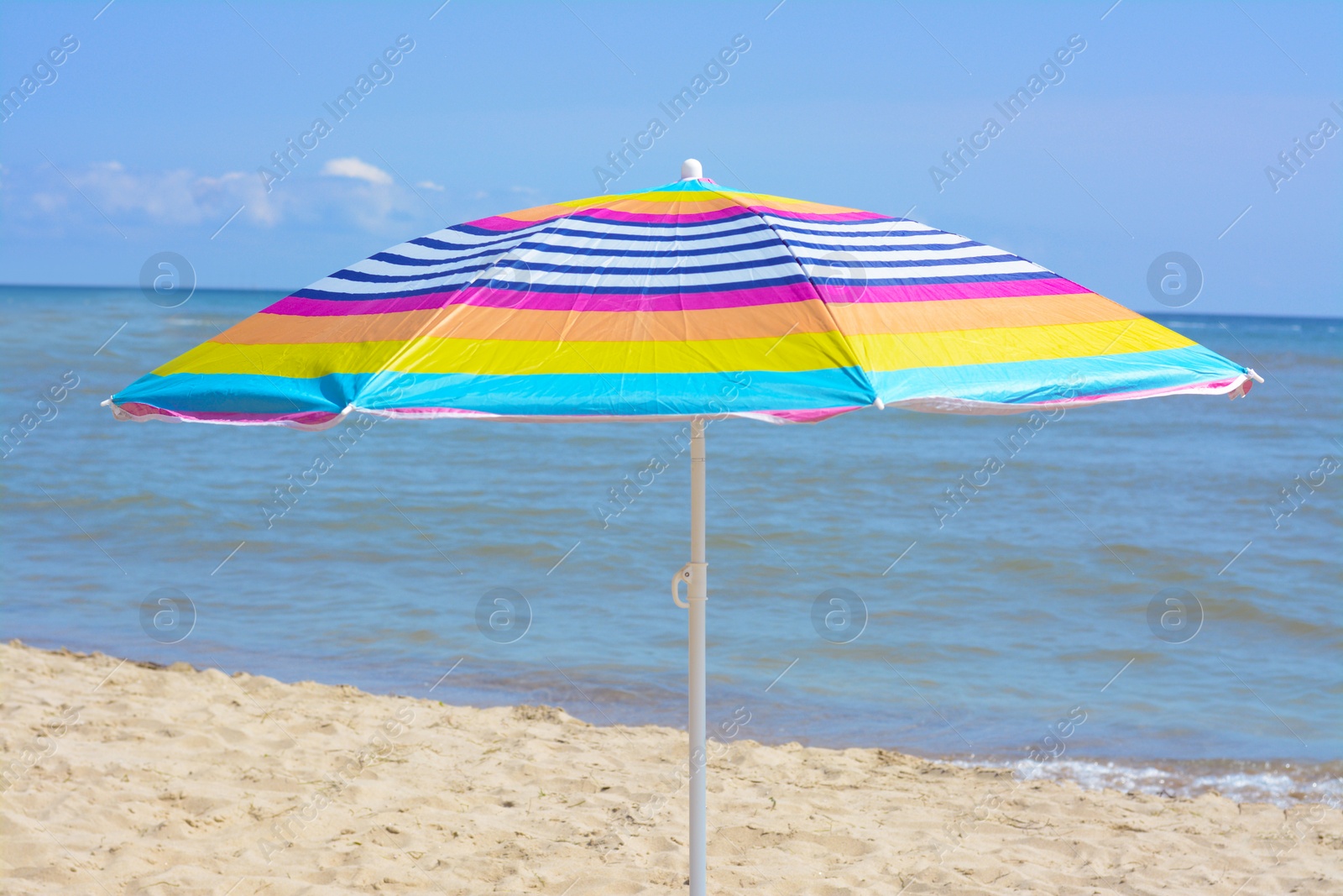 Photo of Colorful striped umbrella on beach near sea