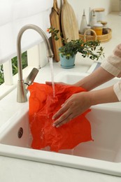 Woman washing beeswax food wrap under tap water in kitchen sink, closeup